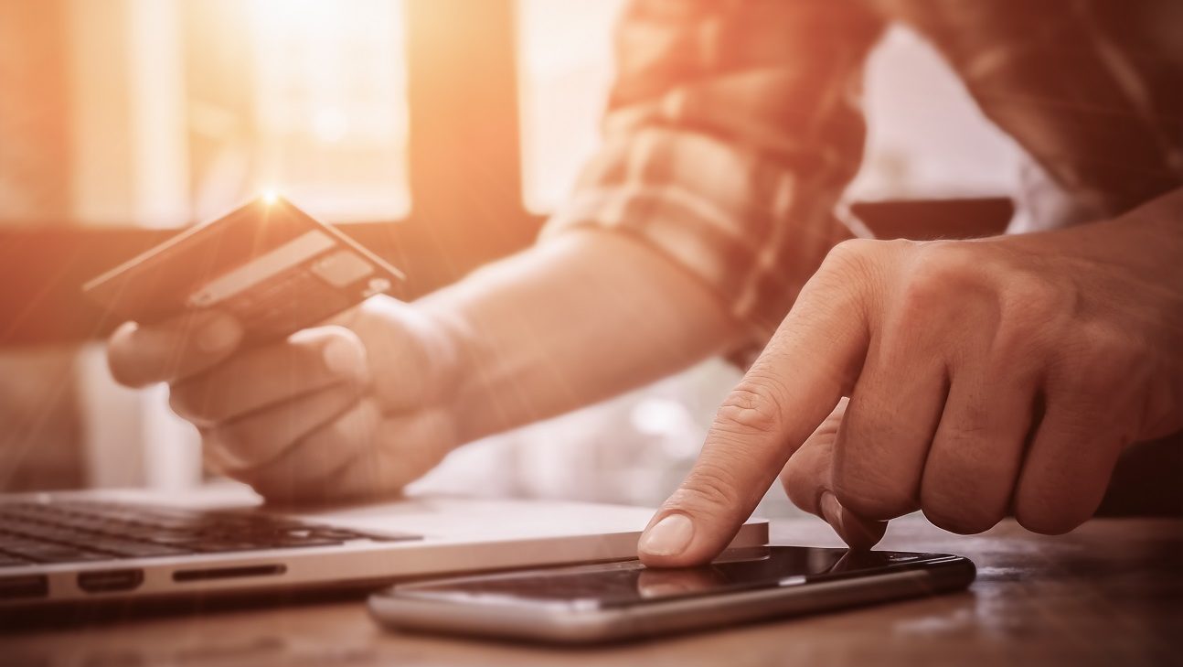 Hands holding credit card and inserting card information onto computer and phone indicating tax scams done via fake websites.