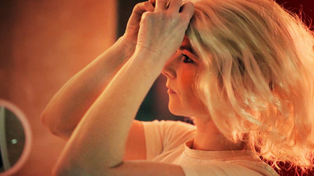 A new cybersecurity training video about online impersonation. A woman puts on a wig.