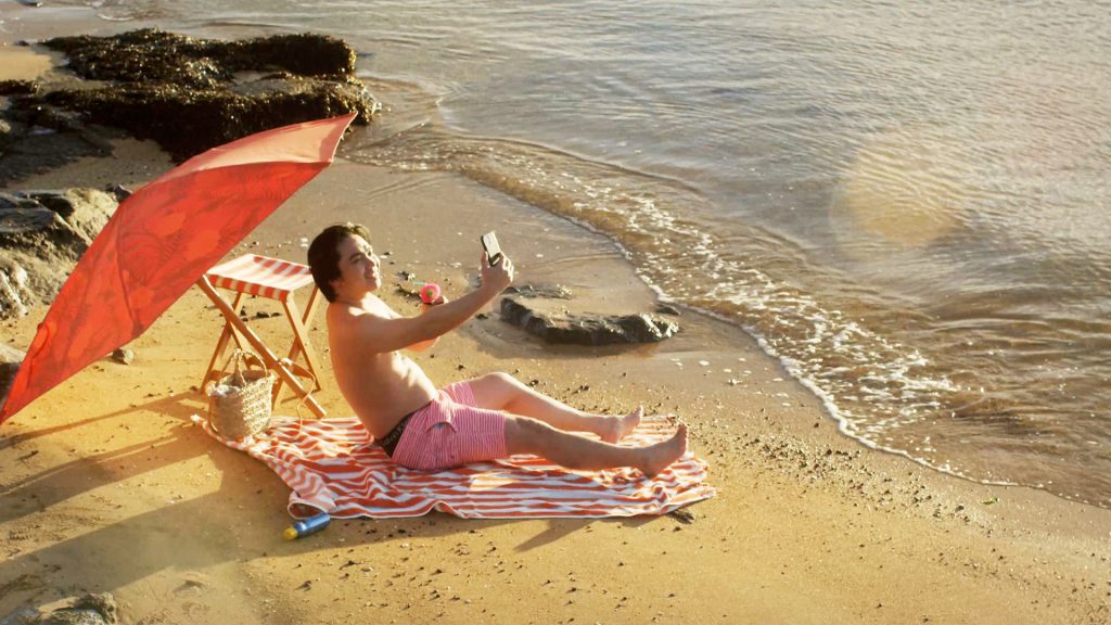 Man on beach at sunset sharing vacation on social media through smartphone.
