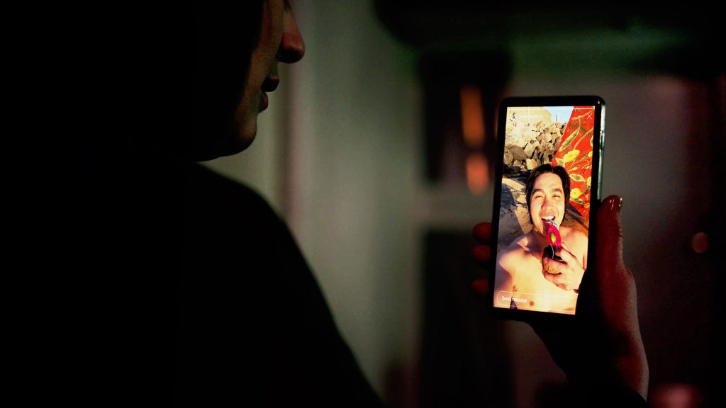 Hacker or burglar watching man on vacation through social media on a smart phone. Sharing on social media is a vacation risk.