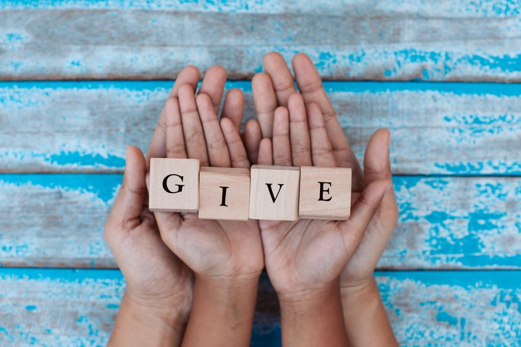 Caucasian hands of a grown up and a child holding wood blocks that spell out "give" on a blue wooden background. Indicating disaster cyber security attacks around donations after a catastrophe.